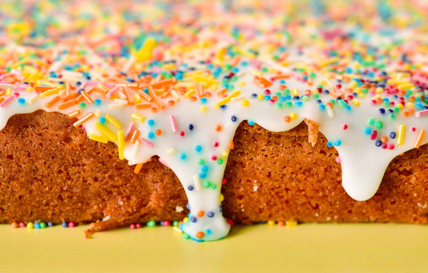 Close up photo of Old Skool Sponge, with icing dripping, covered in multi coloured hundreds and thousands